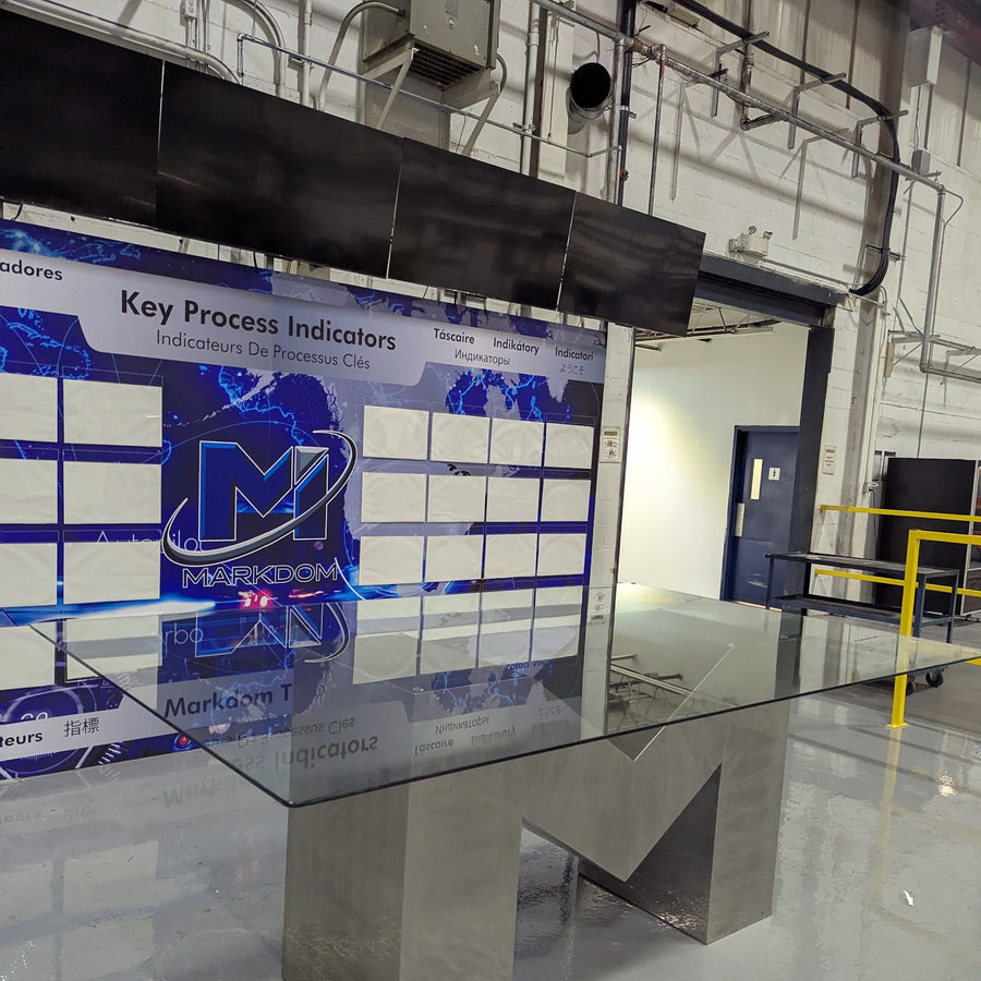 KPI wall with an M-shaped glass meeting table in front, in a plant